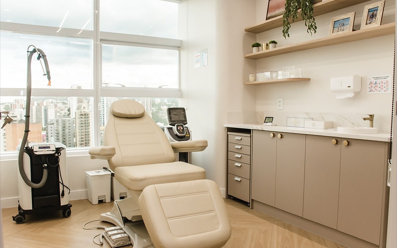 Sala de procedimento com maca e equipamento de dermatologia, com vista da cidade